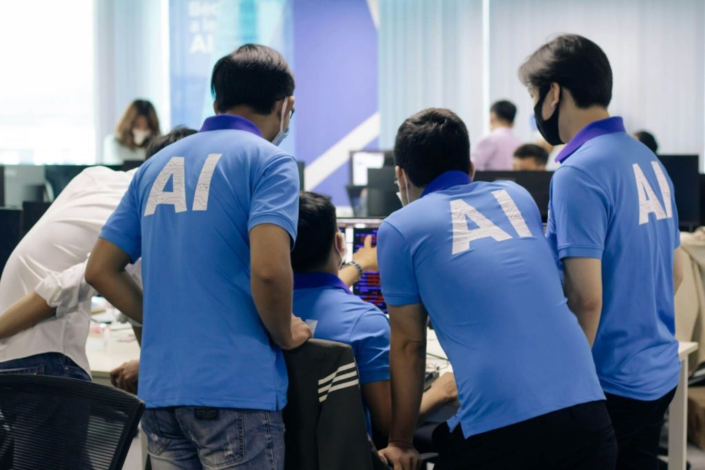 Personas con remera de AI rodean a una persona frente a una computadora